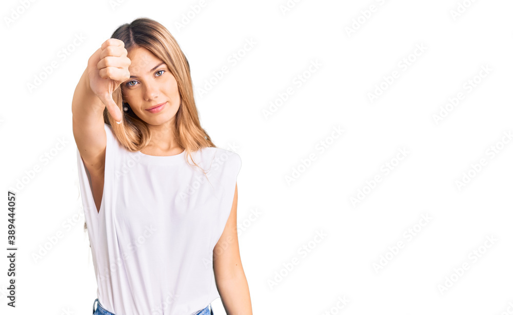 Beautiful caucasian woman with blonde hair wearing casual white tshirt looking unhappy and angry showing rejection and negative with thumbs down gesture. bad expression. Beautiful caucasian woman with blonde hair wearing casual white tshirt looking unhappy and angry showing rejection and negative with thumbs down gesture. bad expression.