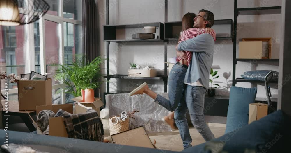Excited family couple young man woman getting settled moving house embracing and spinning around new apartment living room. Life event. Happiness. Cozy home. Excited family couple young man woman getting settled moving house embracing and spinning around new apartment living room. Life event. Happiness. Cozy home.