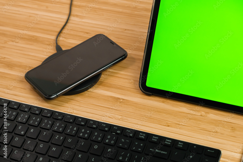 Smart phone is charging on wireless charging next to the tablet with chromo key and keyboard. Smart phone is charging on wireless charging next to the tablet with chromo key and keyboard.
