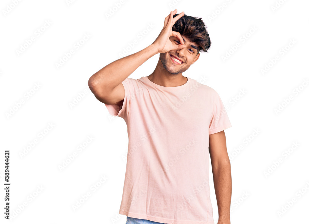 Young hispanic man wearing casual clothes smiling happy doing ok sign with hand on eye looking through fingers Young hispanic man wearing casual clothes smiling happy doing ok sign with hand on eye looking through fingers