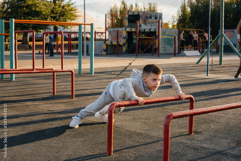 Fototapeta premium A little boy doing push-UPS on the Playground during sunset. Sports, healthy lifestyle
