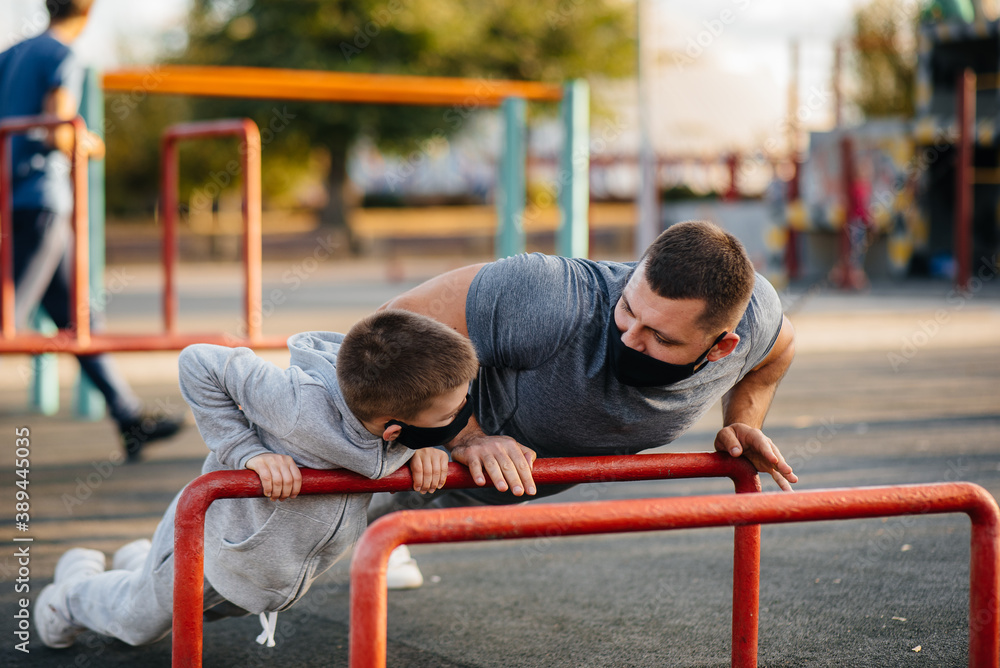 Fototapeta premium Father and son play sports on the sports field in masks during sunset. Healthy parenting and healthy lifestyle