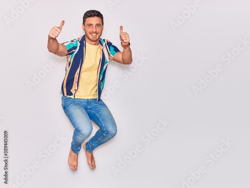 Young handsome hispanic man wearing casual clothes smiling happy. Jumping with smile on face doing ok sign with thumbs up over isolated white background