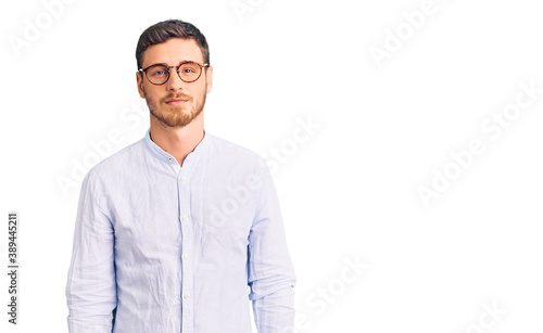 Handsome young man with bear wearing elegant business shirt and glasses relaxed with serious expression on face. simple and natural looking at the camera.