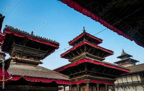 The rooftops of Durbar Square in Kathmandu, Nepal. There are plenty of pigeons flying around, and sitting on the rooftops. Each rooftop is ornated with red and golden ribbon. UNESCO heritage list.