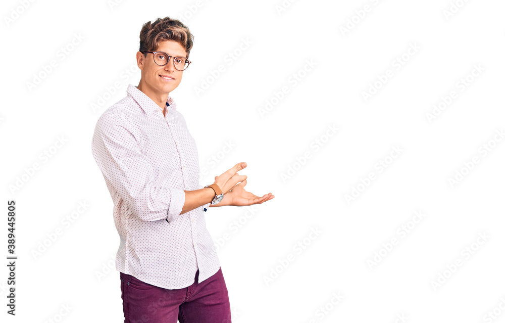 Young handsome man wearing business clothes and glasses inviting to enter smiling natural with open hand