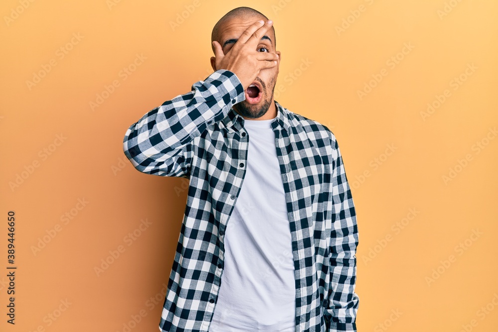 Hispanic adult man wearing casual clothes peeking in shock covering face and eyes with hand, looking through fingers afraid Hispanic adult man wearing casual clothes peeking in shock covering face and eyes with hand, looking through fingers afraid