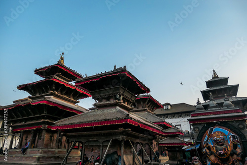 The rooftops of Durbar Square in Kathmandu, Nepal. There are plenty of pigeons flying around, and sitting on the rooftops. Each rooftop is ornated with red and golden ribbon. UNESCO heritage list.