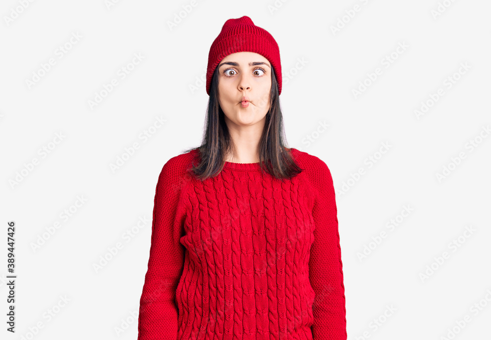 Young beautiful girl wearing sweater and wool cap making fish face with lips, crazy and comical gesture. funny expression. Young beautiful girl wearing sweater and wool cap making fish face with lips, crazy and comical gesture. funny expression.