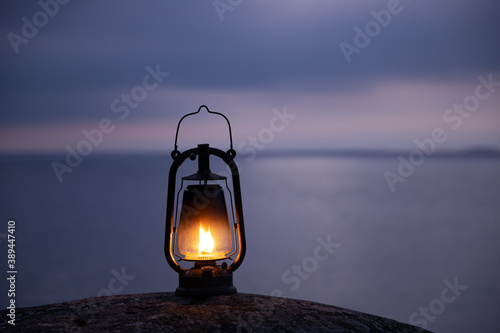 Silhouette of old lantern on the rock. Beautiful cloudy sunset sky and sea on background. Hurricane lamp soft glow at the seaside. Stormy weather.