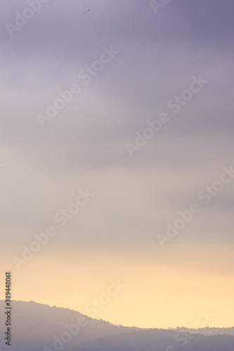 Silhueta de serra distante com céu ao entardecer mesclando tons de rosa, amarelo e púrpura, em estilo minimalista, quase abstrato. © Vernaglia