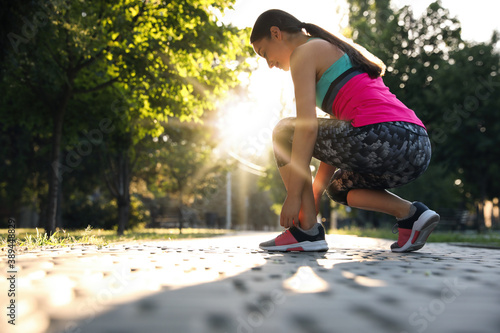 Young woman tying shoelaces before morning run in park. Space for text