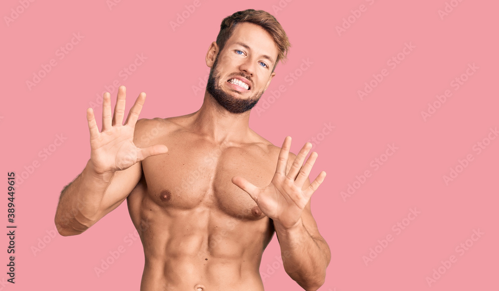 Fototapeta premium Young caucasian man standing shirtless afraid and terrified with fear expression stop gesture with hands, shouting in shock. panic concept.