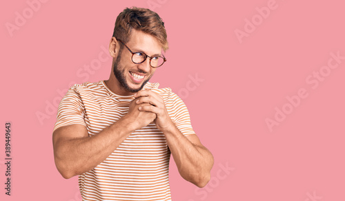 Young caucasian man wearing casual clothes and glasses laughing nervous and excited with hands on chin looking to the side