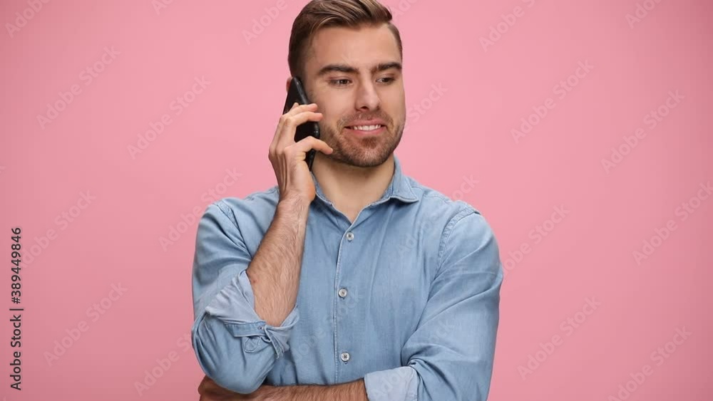 attractive casual guy in jeans shirt talking on the phone, pointing fingers and making telephone gesture on pink background in studio attractive casual guy in jeans shirt talking on the phone, pointing fingers and making telephone gesture on pink background in studio
