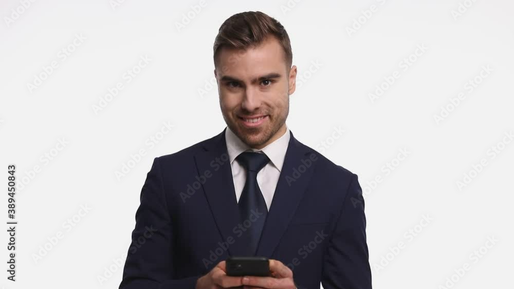 young businessman in navy blue suit holding cellphone and texting, smiling and nodding, standing isolated on white background young businessman in navy blue suit holding cellphone and texting, smiling and nodding, standing isolated on white background
