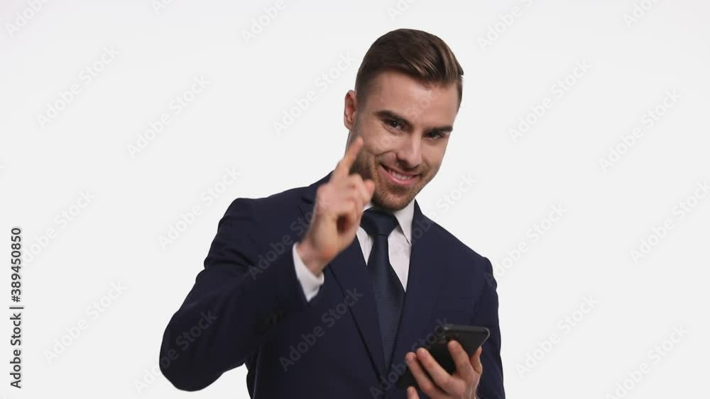 smiling businessman in navy blue suit texting, reading emails on the phone, pointing fingers and smiling, standing isolated on white background in studio smiling businessman in navy blue suit texting, reading emails on the phone, pointing fingers and smiling, standing isolated on white background in studio