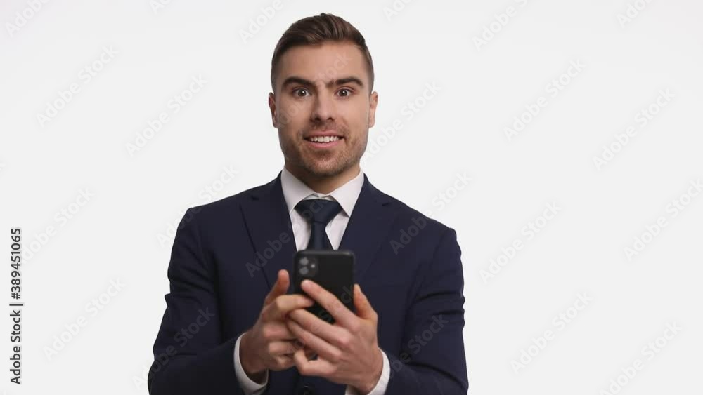 excited handsome man in navy blue suit holding phone, reading emails in a surprised manner, holding arms up and dancing, laughing and jumping isolated on white background in studio excited handsome man in navy blue suit holding phone, reading emails in a surprised manner, holding arms up and dancing, laughing and jumping isolated on white background in studio