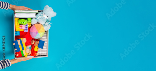Donation concept. Kid hands with donate box with clothes, books and toys on light blue background. Top view