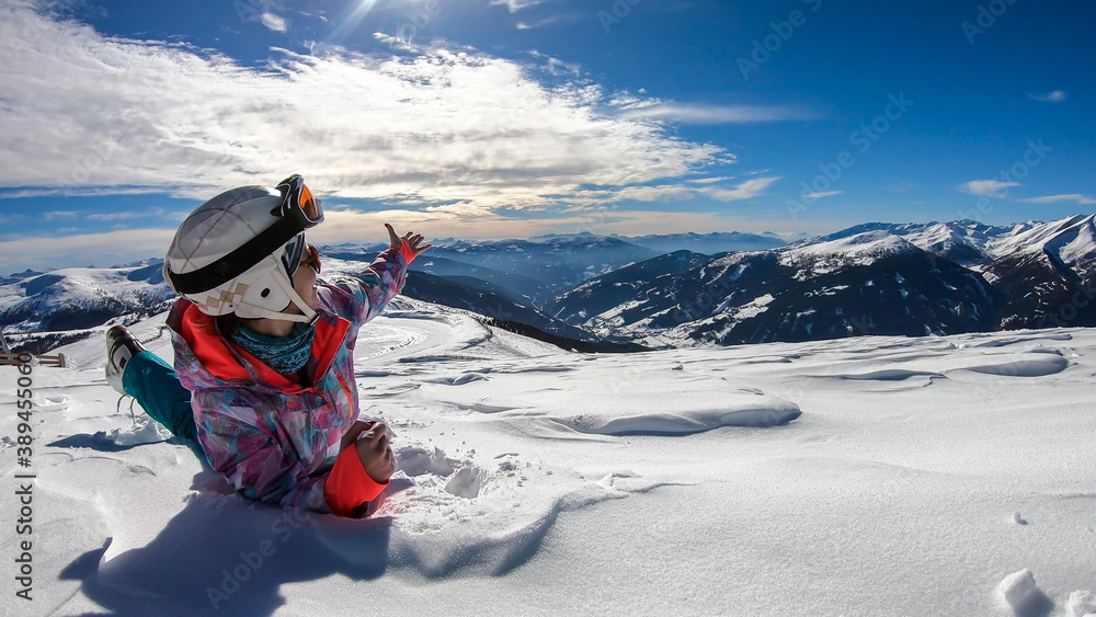 A woman lying in powder snow any enjoying the sun on top of Katschberg in Austria. She is happy and joyful. Panoramic view on the surrounding mountains. Winter wonderland, Clear and sunny winter day