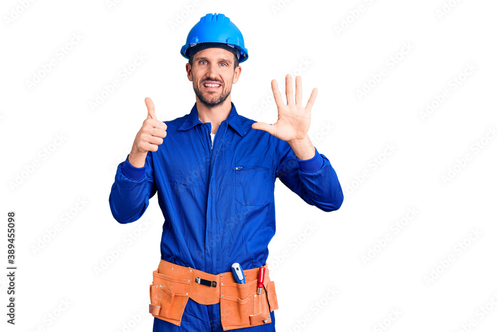 Young handsome man wearing worker uniform and hardhat showing and pointing up with fingers number six while smiling confident and happy.