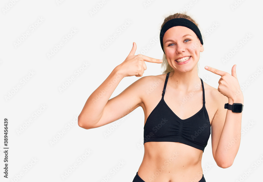 Young beautiful blonde woman wearing sportswear smiling cheerful showing and pointing with fingers teeth and mouth. dental health concept. Young beautiful blonde woman wearing sportswear smiling cheerful showing and pointing with fingers teeth and mouth. dental health concept.