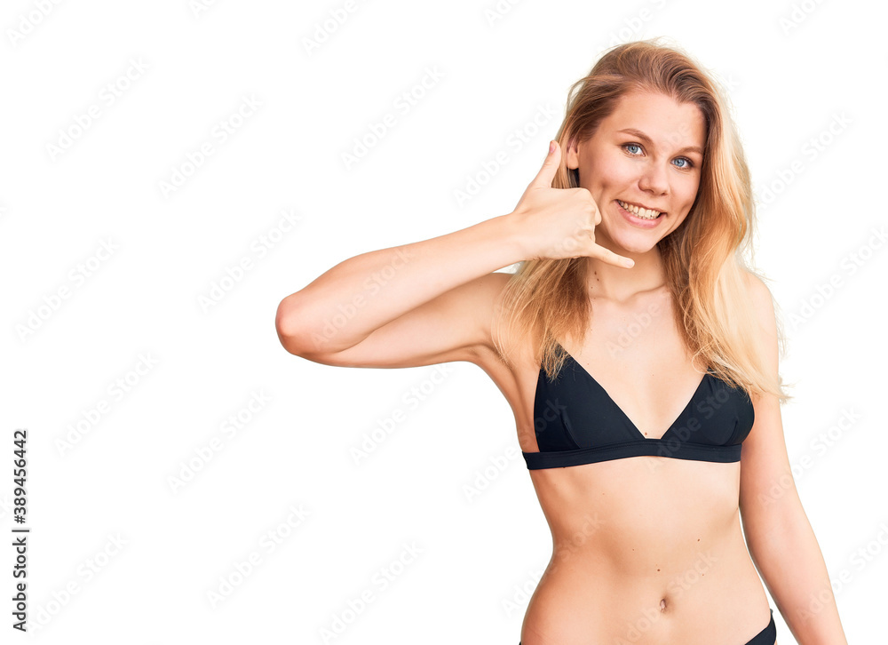 Young beautiful blonde woman wearing bikini smiling doing phone gesture with hand and fingers like talking on the telephone. communicating concepts. Young beautiful blonde woman wearing bikini smiling doing phone gesture with hand and fingers like talking on the telephone. communicating concepts.