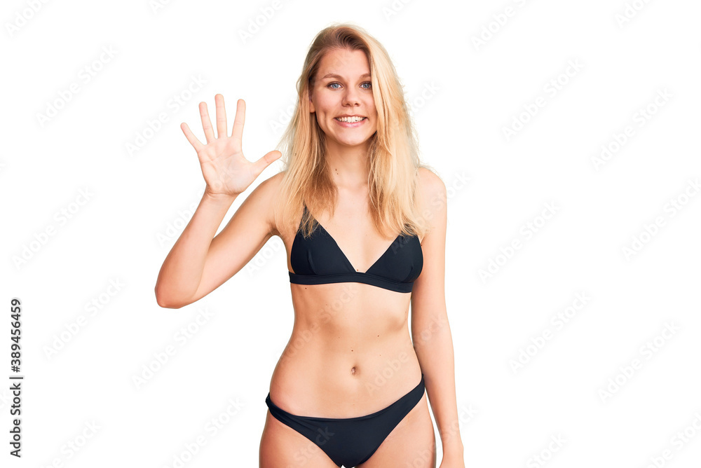 Young beautiful blonde woman wearing bikini showing and pointing up with fingers number five while smiling confident and happy. Young beautiful blonde woman wearing bikini showing and pointing up with fingers number five while smiling confident and happy.