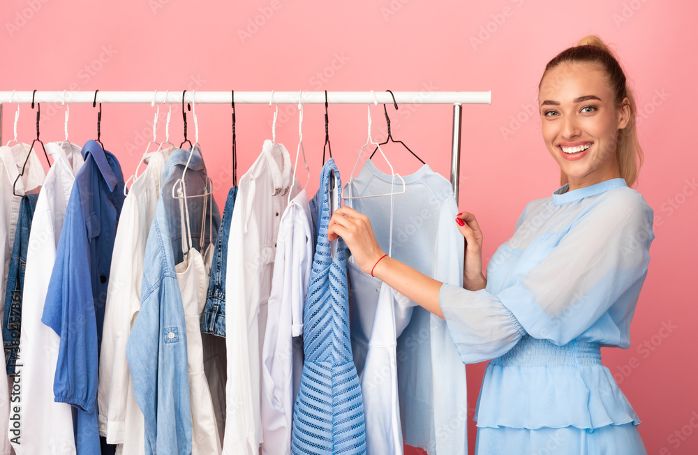 Young lady choosing clothes standing near rack