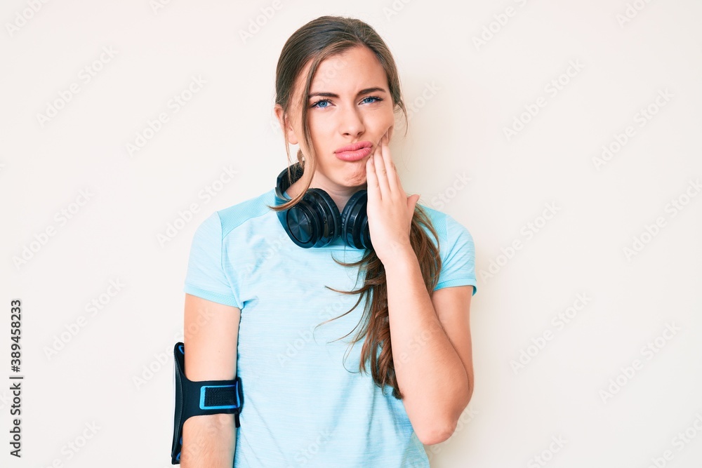 Beautiful young caucasian woman wearing gym clothes and using headphones touching mouth with hand with painful expression because of toothache or dental illness on teeth. dentist Beautiful young caucasian woman wearing gym clothes and using headphones touching mouth with hand with painful expression because of toothache or dental illness on teeth. dentist