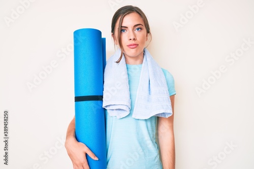 Fotografie Beautiful young caucasian woman holding yoga mat thinking attitude and sober exp