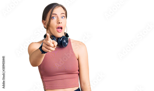 Beautiful caucasian young woman wearing gym clothes and using headphones pointing displeased and frustrated to the camera, angry and furious with you
