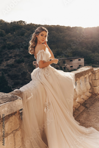 beautiful bride with blond hair in luxurious wedding dress posing in balcony with beautiful view of mountains and sea photo