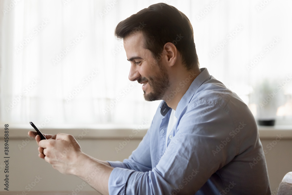 Good day. Happy smiling young man reading fun message from gadget screen, making answering video call by smartphone, texting chatting with friend, making purchase buying goods services in online shop Good day. Happy smiling young man reading fun message from gadget screen, making answering video call by smartphone, texting chatting with friend, making purchase buying goods services in online shop
