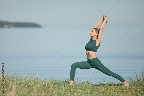 Woman in green sportswear practices yoga by sea