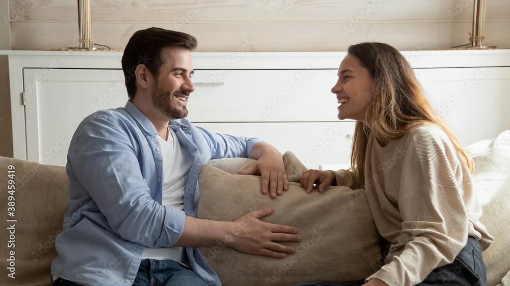 Resting at home together. Pleasant young millennial family couple, brother and sister, diverse friends sitting on cozy sofa at living room relaxing together talking joking having cheerful conversation Resting at home together. Pleasant young millennial family couple, brother and sister, diverse friends sitting on cozy sofa at living room relaxing together talking joking having cheerful conversation