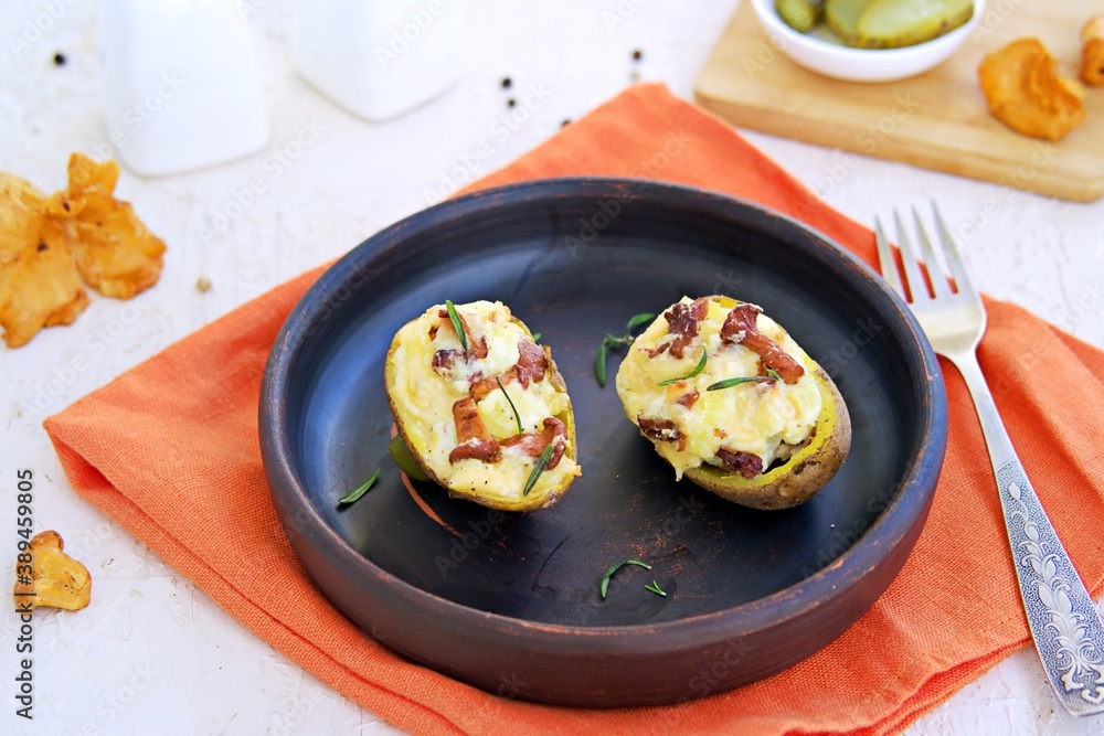 Twice baked potatoes with cheese and chanterelle mushrooms on a brown clay plate on a light concrete background. Recipes with potatoes. Twice baked potatoes with cheese and chanterelle mushrooms on a brown clay plate on a light concrete background. Recipes with potatoes.