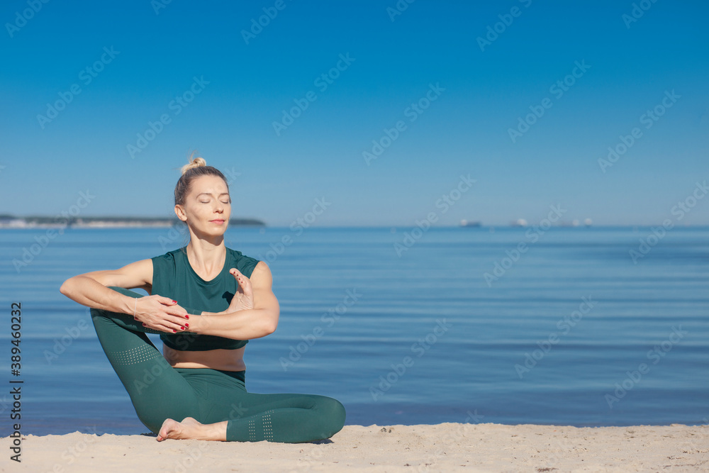 Woman in green sportswear practices yoga by sea