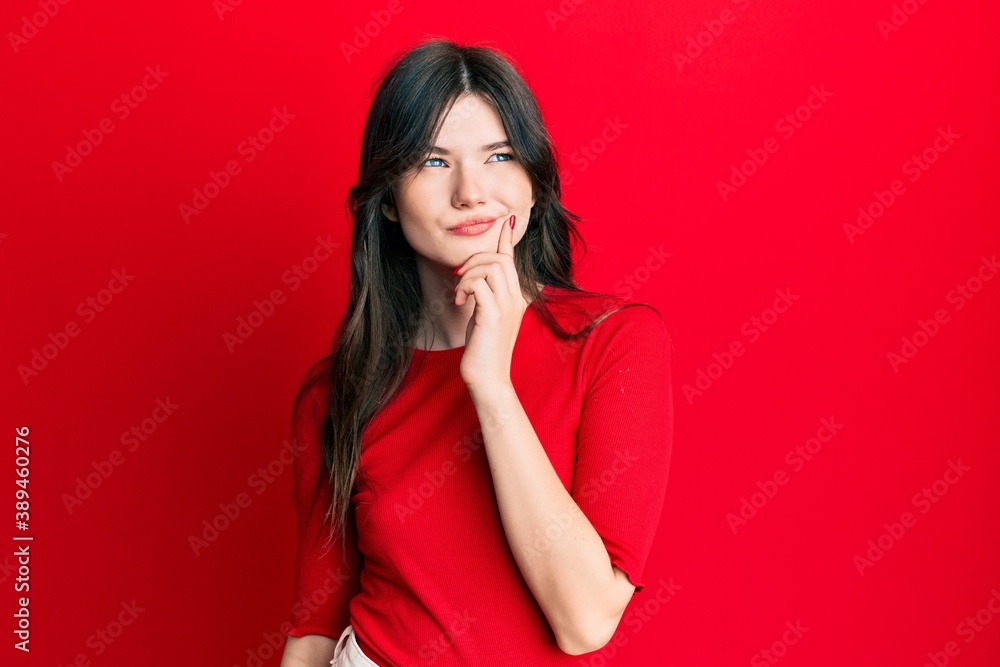 Young beautiful caucasian girl wearing casual red shirt thinking concentrated about doubt with finger on chin and looking up wondering Young beautiful caucasian girl wearing casual red shirt thinking concentrated about doubt with finger on chin and looking up wondering
