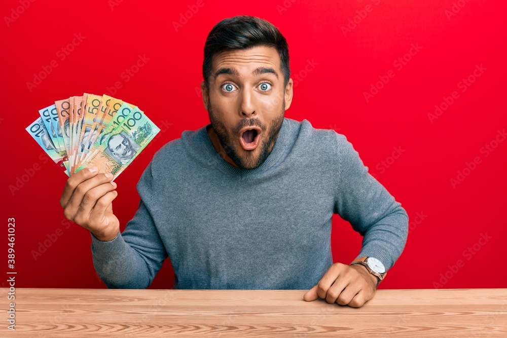 Handsome hispanic man holding australian dollars scared and amazed with open mouth for surprise, disbelief face Handsome hispanic man holding australian dollars scared and amazed with open mouth for surprise, disbelief face