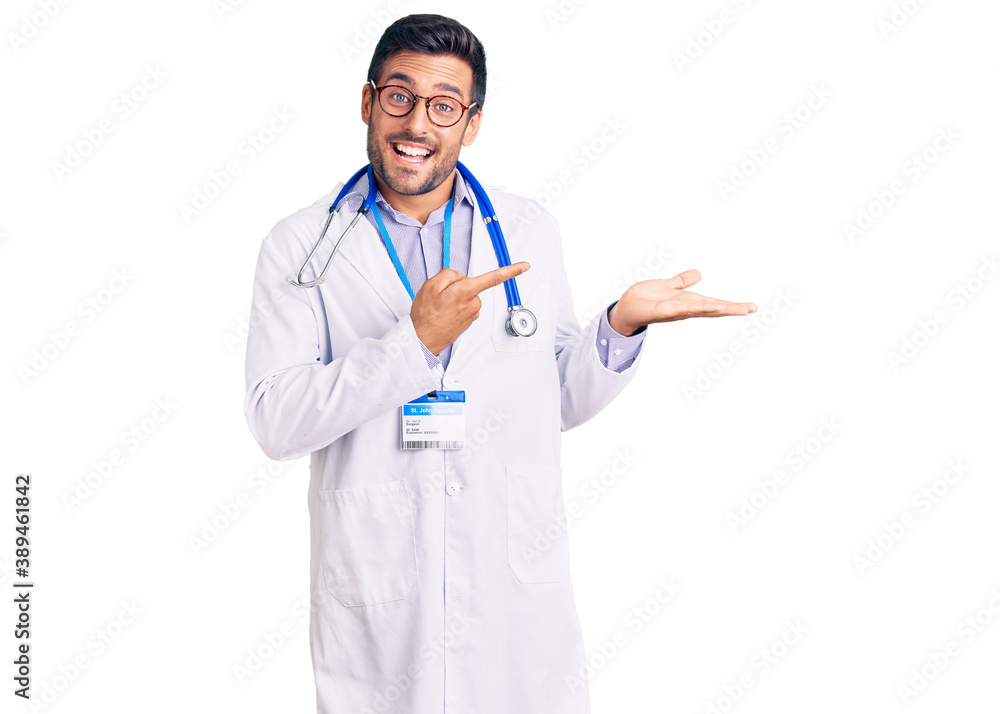 Young hispanic man wearing doctor uniform and stethoscope amazed and smiling to the camera while presenting with hand and pointing with finger. Young hispanic man wearing doctor uniform and stethoscope amazed and smiling to the camera while presenting with hand and pointing with finger.