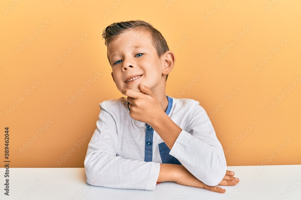 Adorable caucasian kid wearing casual clothes sitting on the table with hand on chin thinking about question, pensive expression. smiling with thoughtful face. doubt concept. Adorable caucasian kid wearing casual clothes sitting on the table with hand on chin thinking about question, pensive expression. smiling with thoughtful face. doubt concept.