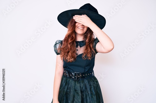 Young beautiful woman wearing witch halloween costume smiling and laughing with hand on face covering eyes for surprise. blind concept. © Krakenimages.com