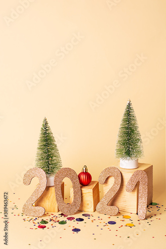 New year creative concept. New year 2021 golden numbers and two artificial Christmas trees, red  decoration on wooden cubes and multicolored confetti around on a beige background. Christmas background