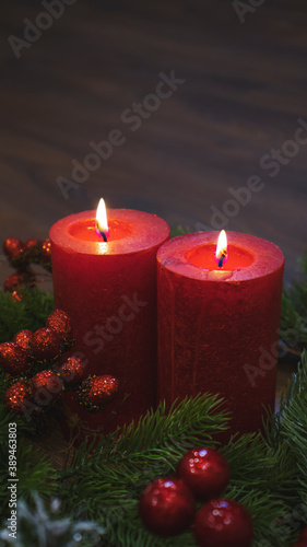 Red candles with fir branches and a toy pine cone. Dark Christmas and New Year background. Red candles  green spruce branches  red berries.