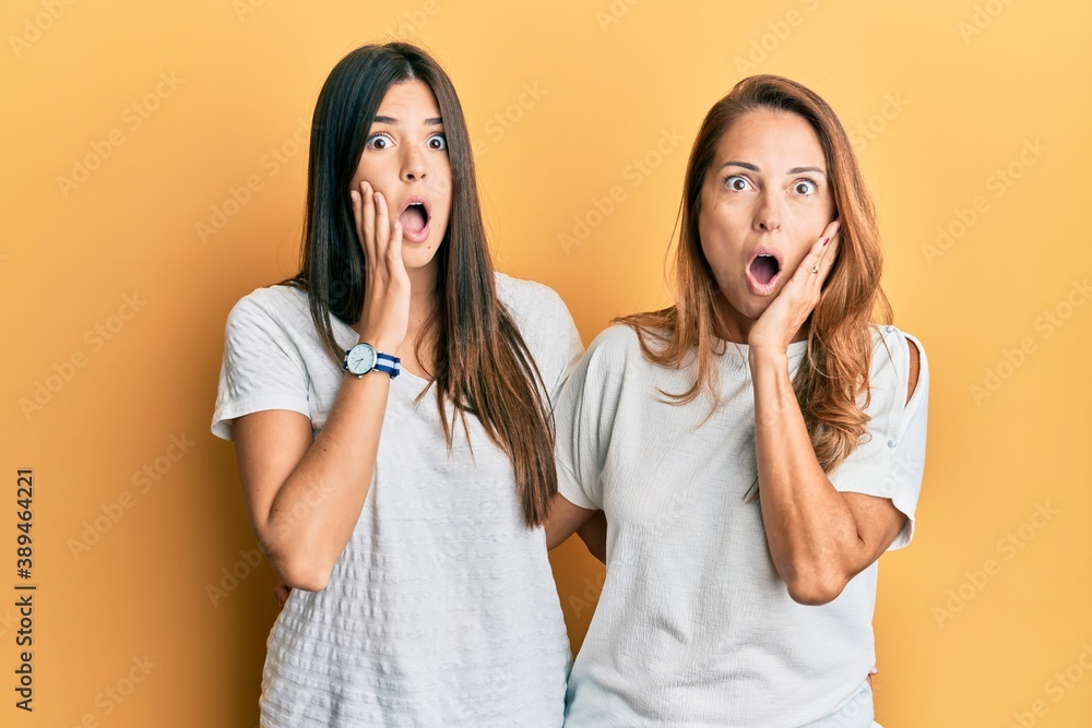 Hispanic family of mother and daughter wearing casual white tshirt afraid and shocked, surprise and amazed expression with hands on face Hispanic family of mother and daughter wearing casual white tshirt afraid and shocked, surprise and amazed expression with hands on face