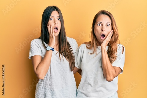 Hispanic family of mother and daughter wearing casual white tshirt afraid and shocked, surprise and amazed expression with hands on face