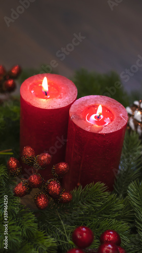 Red candles with fir branches and a toy pine cone. Dark Christmas and New Year background. Red candles, green spruce branches, red berries.