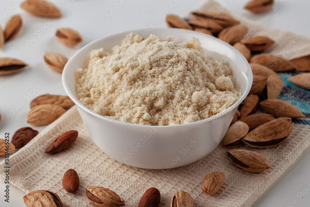 Almond nuts and almond flour in a plate are on a white table Almond nuts and almond flour in a plate are on a white table