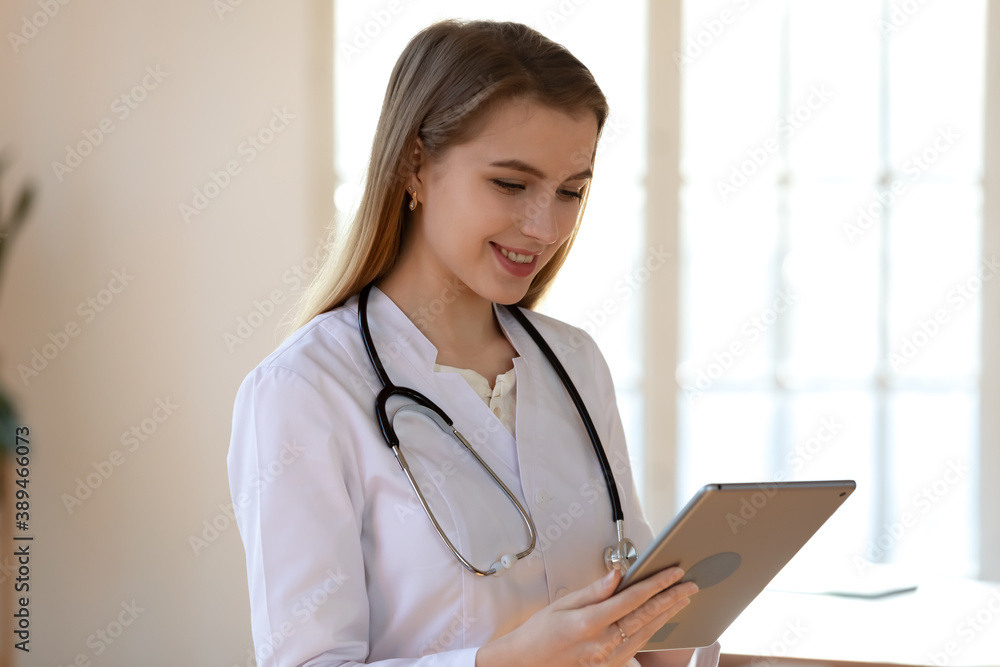 Modern doctor. Responsible smiling young woman gp clinic therapist connecting with colleagues physicians specialists by video conference using pad asking advice about diagnosis or prescription details Modern doctor. Responsible smiling young woman gp clinic therapist connecting with colleagues physicians specialists by video conference using pad asking advice about diagnosis or prescription details